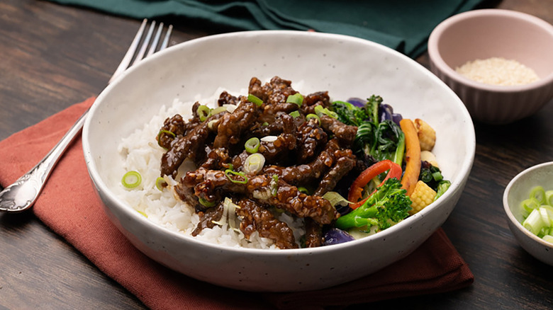 Bowl of spicy sesame beef with rice and stir-fried vegetables