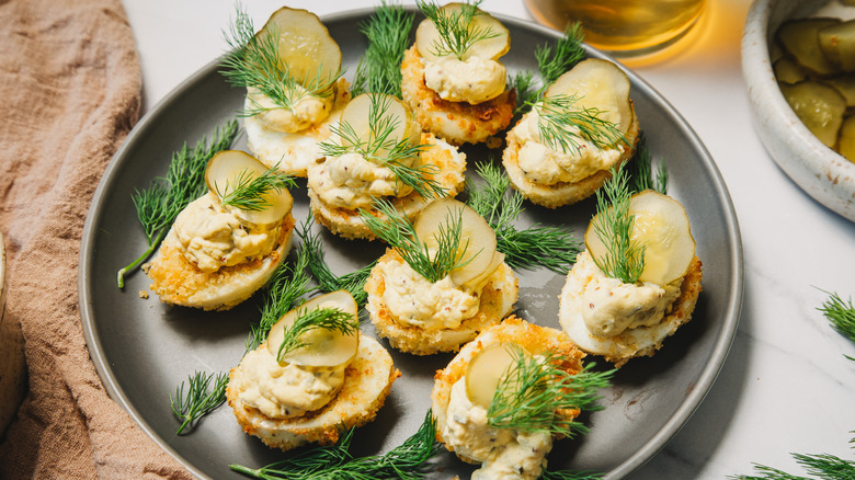 Pickle and dill topped deviled eggs on a grey plate.