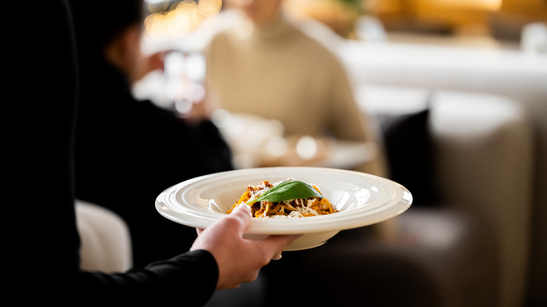 A server carrying a pasta dish with blurred restaurant in the background