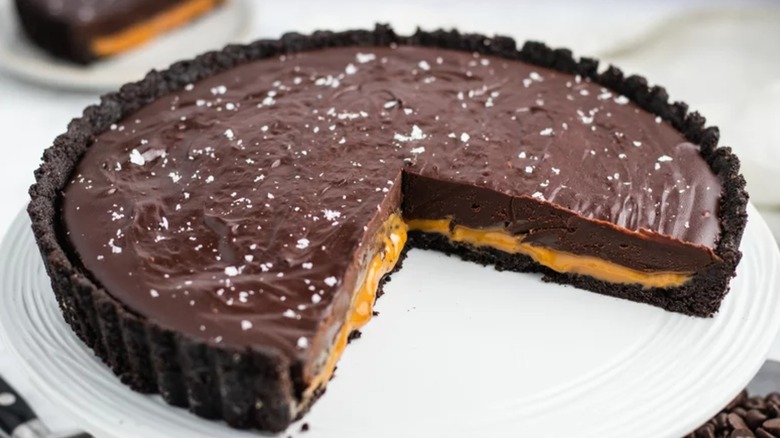 Chocolate caramel tart with slice missing on white platter