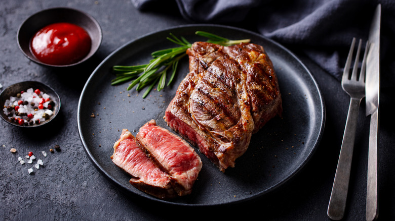 Grilled steak cooked medium rare, served on a black plate with two slices cut