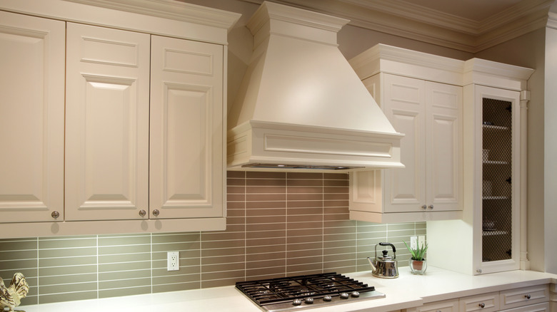 white kitchen with a white range hood over a stove, with cabinets around