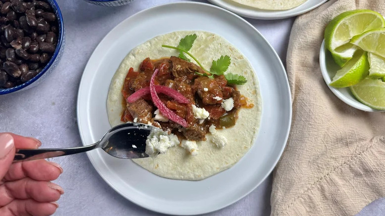 Spooning crumbled cotija cheese onto a carne picada beef taco