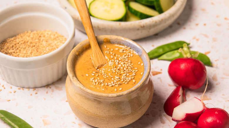 Sesame dressing in small bowl with spoon with radishes and cucumbers.