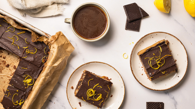 Two slices of chocolate lemon bars alongside a coffee and the tray of bars