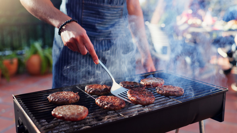 Person grilling burger patties over charcoal