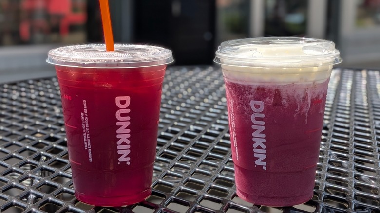 Two purple Dunkin' drinks on a black outdoor picnic table