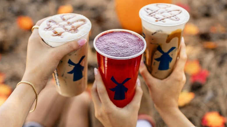 Three people holding Dutch Bros fall seasonal drinks, including caramel pumpkin lattes and red-colored fruit refresher