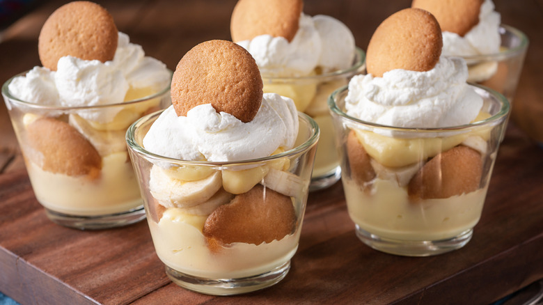 Individual glass cups of banana pudding with banana slices, vanilla wafer cookies, and whipped cream