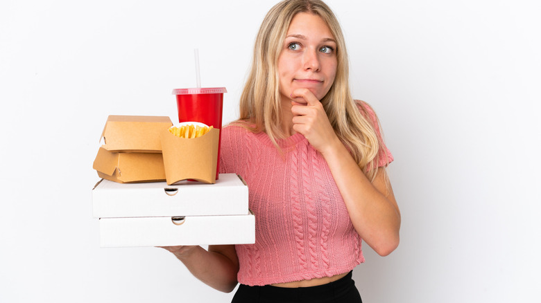 Thoughtful woman holding fast food to-go boxes
