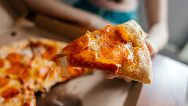 greasy pizza box with person holding slice