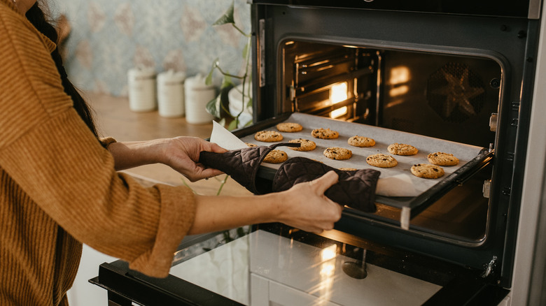 Hands taking tray of cookies out of an oven.
