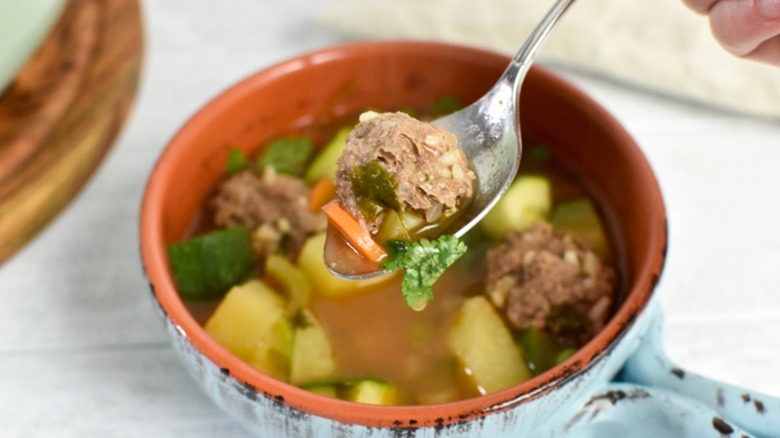 Bowl of Albondigas with a silver spoon lifting a bit of the soup toward the viewer