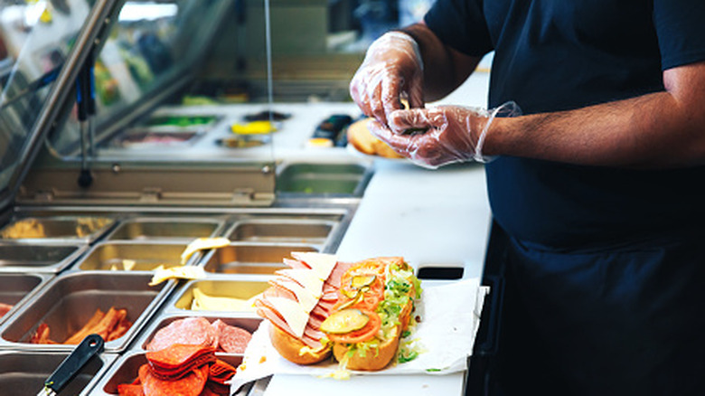 A person assembling a sub sandwich in a fast food restaurant