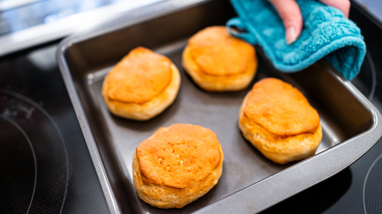 A person is holding a tray of baked Pillsbury biscuits.