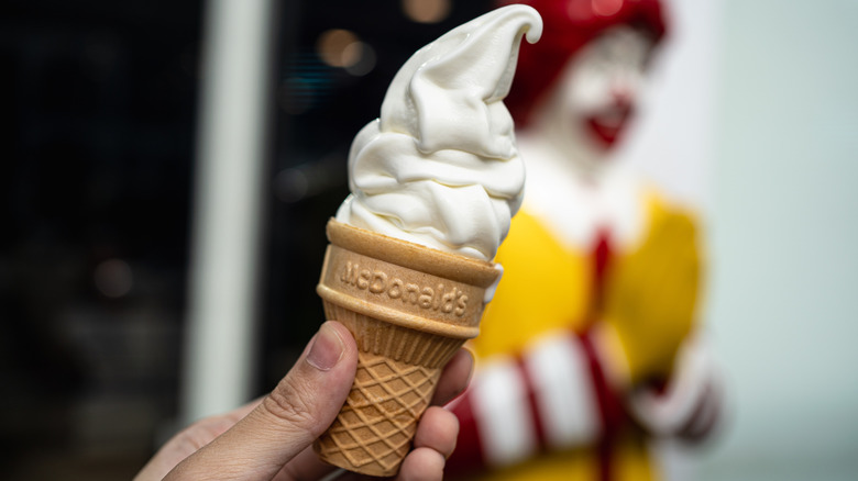A person holding a McDonald's ice cream cone in front of a Ronald McDonald statue