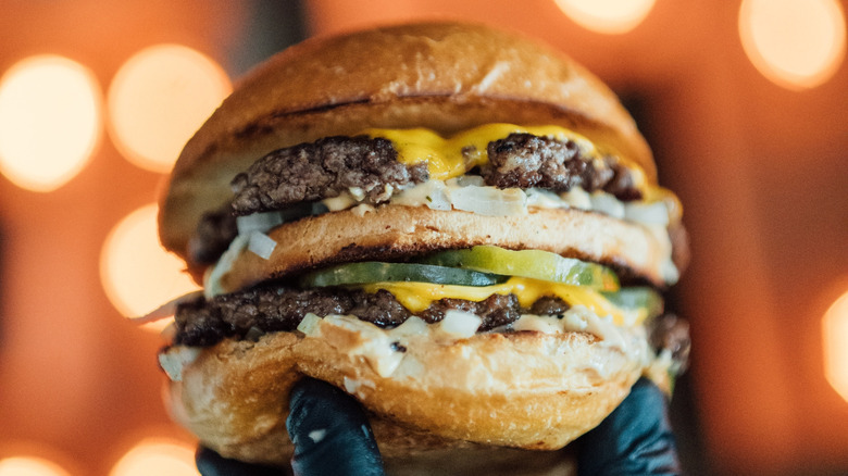 A perfect double decker burger is held up by a gloved hand