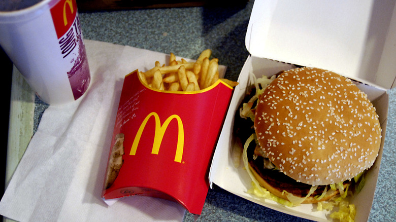 A Big Mac in a cardboard box next to an order of McDonald's fries and a drink