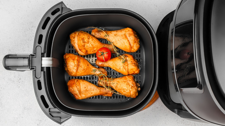 Top view of chicken drumsticks going into black air fryer