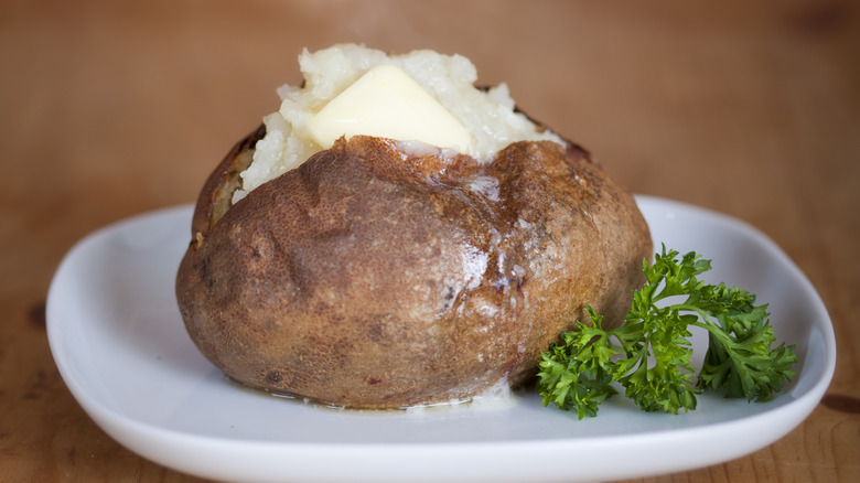 a plain baked potato with butter on a plate with a parsley garnish
