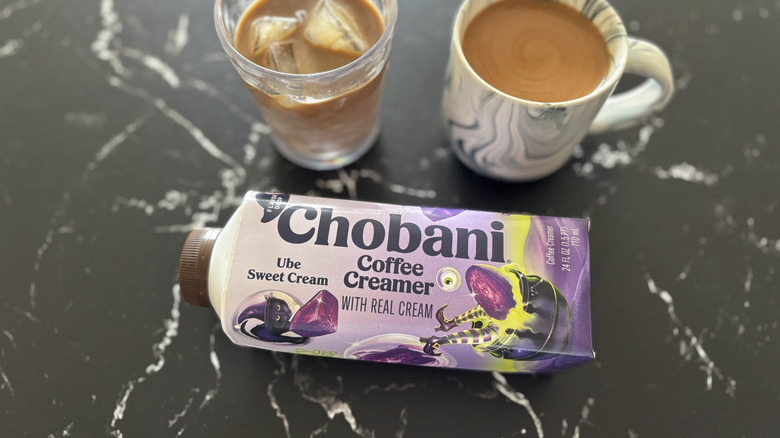 Chobani Ube Sweet Cream coffee creamer bottle with cup of iced and hot coffee in background