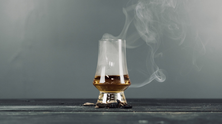 A dramatic shot of a glass of whisky with smoke rising out of the glass