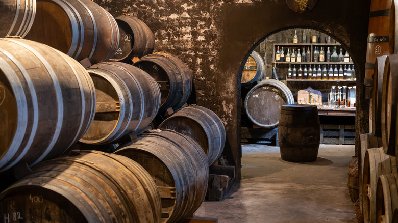 Stacked wooden barrels leading through archway into room with bottles on walls