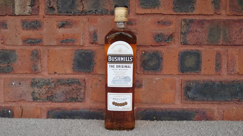 A bottle of Bushmills Original posed in front of a red brick background