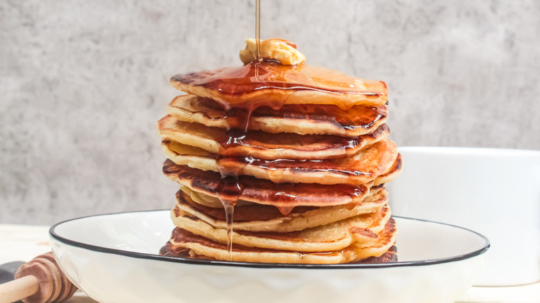 Honey being poured over a stack of thick, fluffy buttermilk pancakes