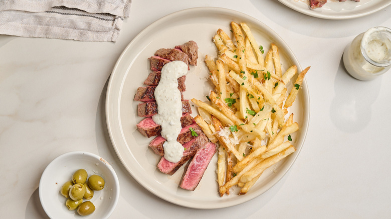 sliced steak on a plate with french fries and a cream sauce