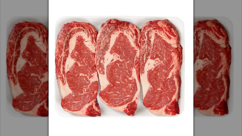 Three Kirkland Signature USDA Prime Ribeye Steaks on white tray on white background