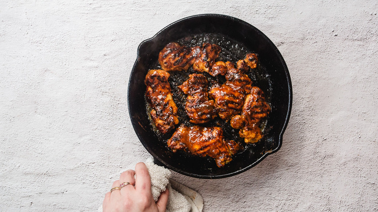 Hand holding cast iron pan with chipotle honey chicken