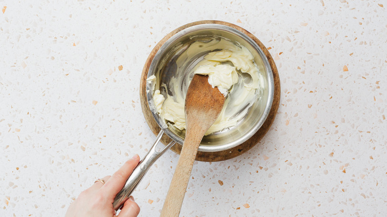 Hand holding saucepan with butter and wooden spoon