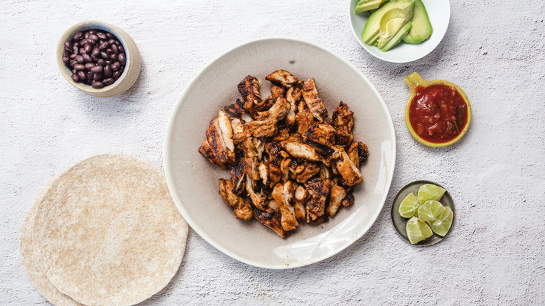 Plate with chipotle honey chicken on plate, tortillas, black beans, limes, salsa and avocado