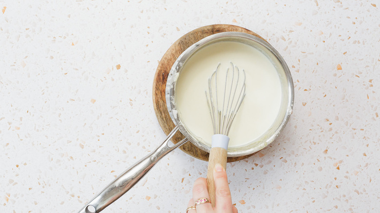 Hand holding saucepan with creamy sauce and whisk