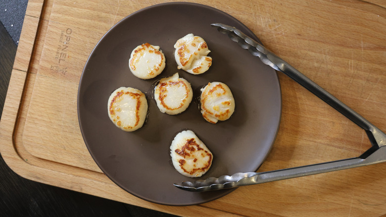 seared scallops on a plate with tongs