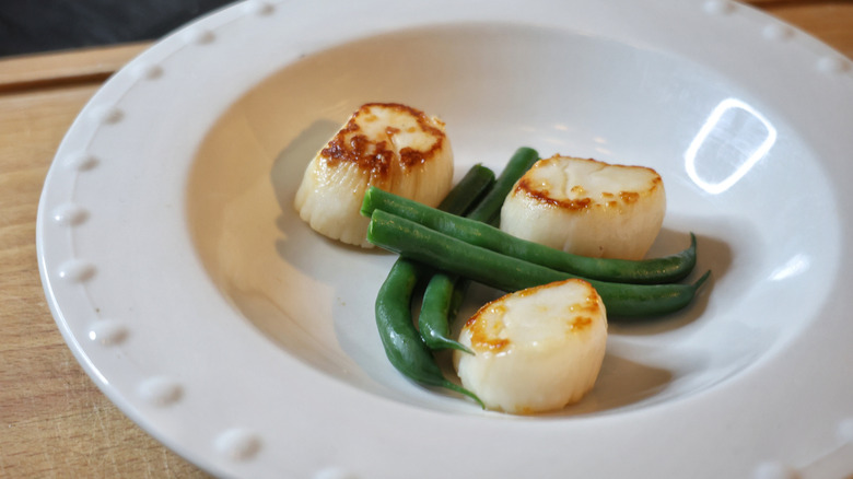 seared scallops and green beans arranged in a shallow bowl