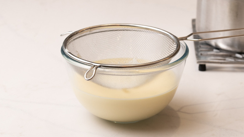 a bowl of custard with a sieve resting over it