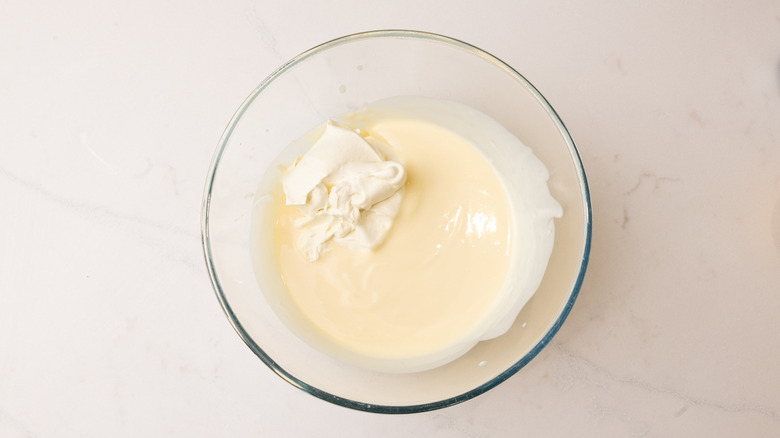 cream added to a glass bowl of custard on marble surface