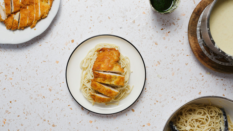Chicken cutlet over pasta on white plate with components around