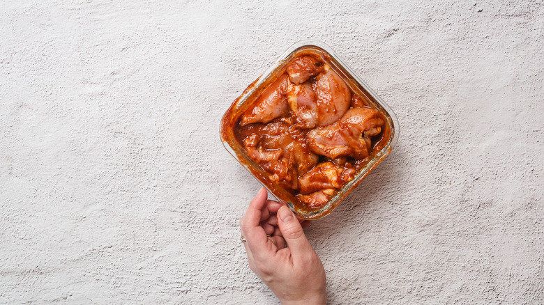 Hand reaching for container with chicken in marinade