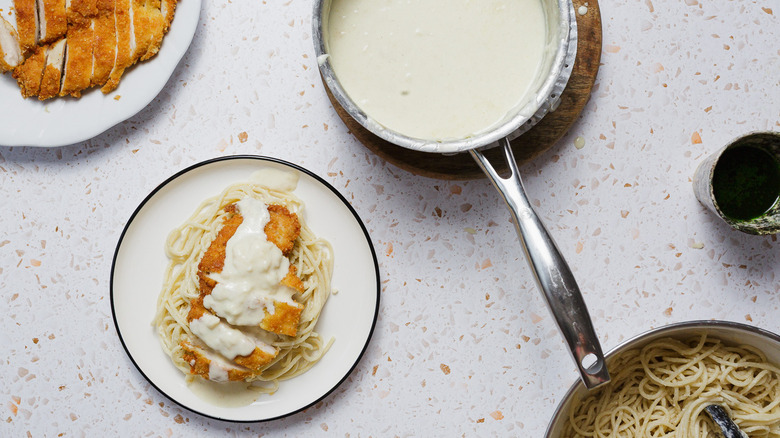 Chicken cutlet over pasta on white plate with sauce with components around