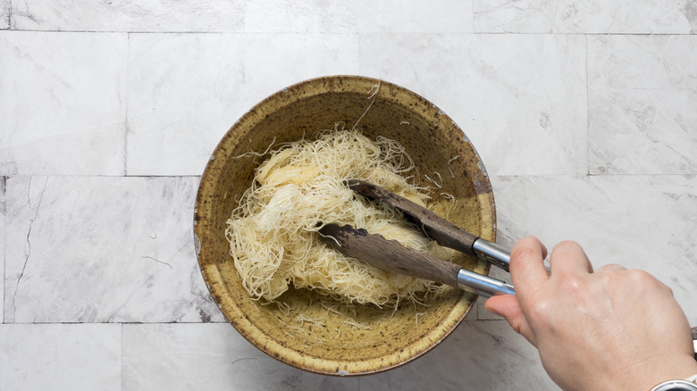 Tossing kataifi noodles with melted butter in bowl