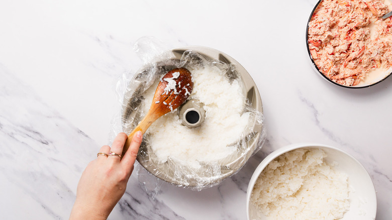adding rice to plastic wrapped bundt cake pan besides spicy crab mix