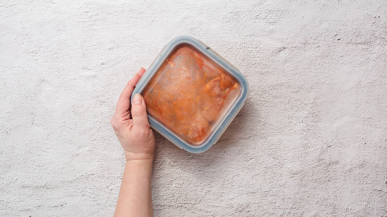 Hand holding sealed container with chicken in marinade