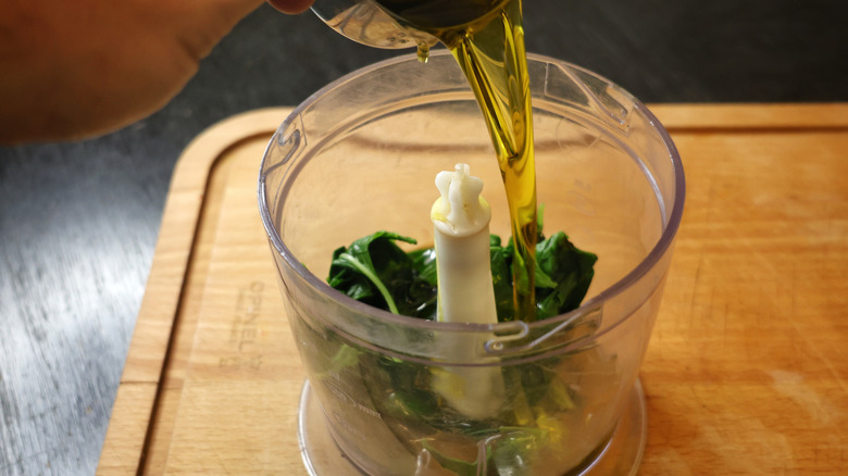 olive oil pouring into food processor with basil in it