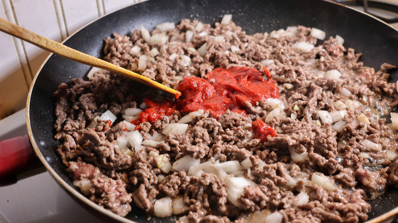 tomato paste atop in skillet of ground beef and onions