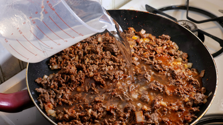 water pouring from measuring cup into skillet of ground beef