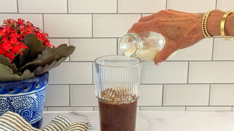 hand adding milk to glass