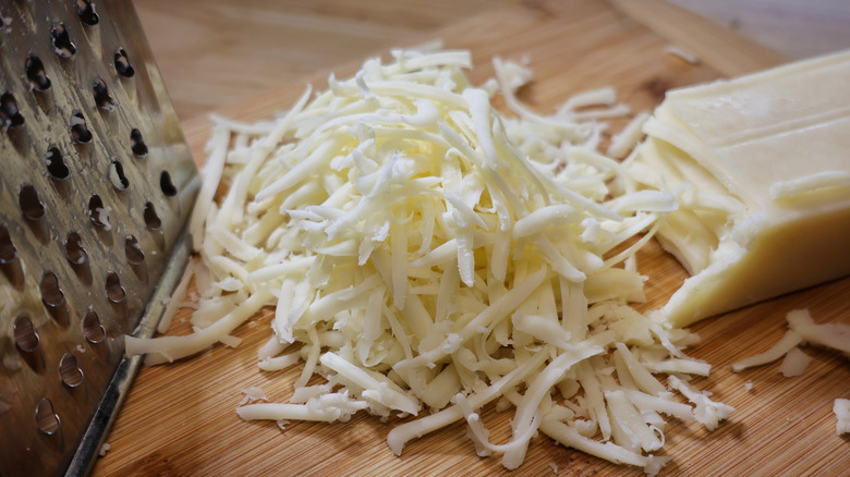 pile of grated mozzarella next to cheese grater and block of cheese
